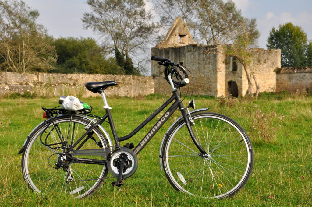 Bicycle on Port Meadow along the River Thames. A historic building. Grassy meadow banks along the river.